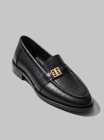Volterra Black - מוקסין עור שחור עם רצועה רחבה בחזית ועיטור מתכתי זהוב, תפר מודגש סביב החרטום וסוליה דקה.