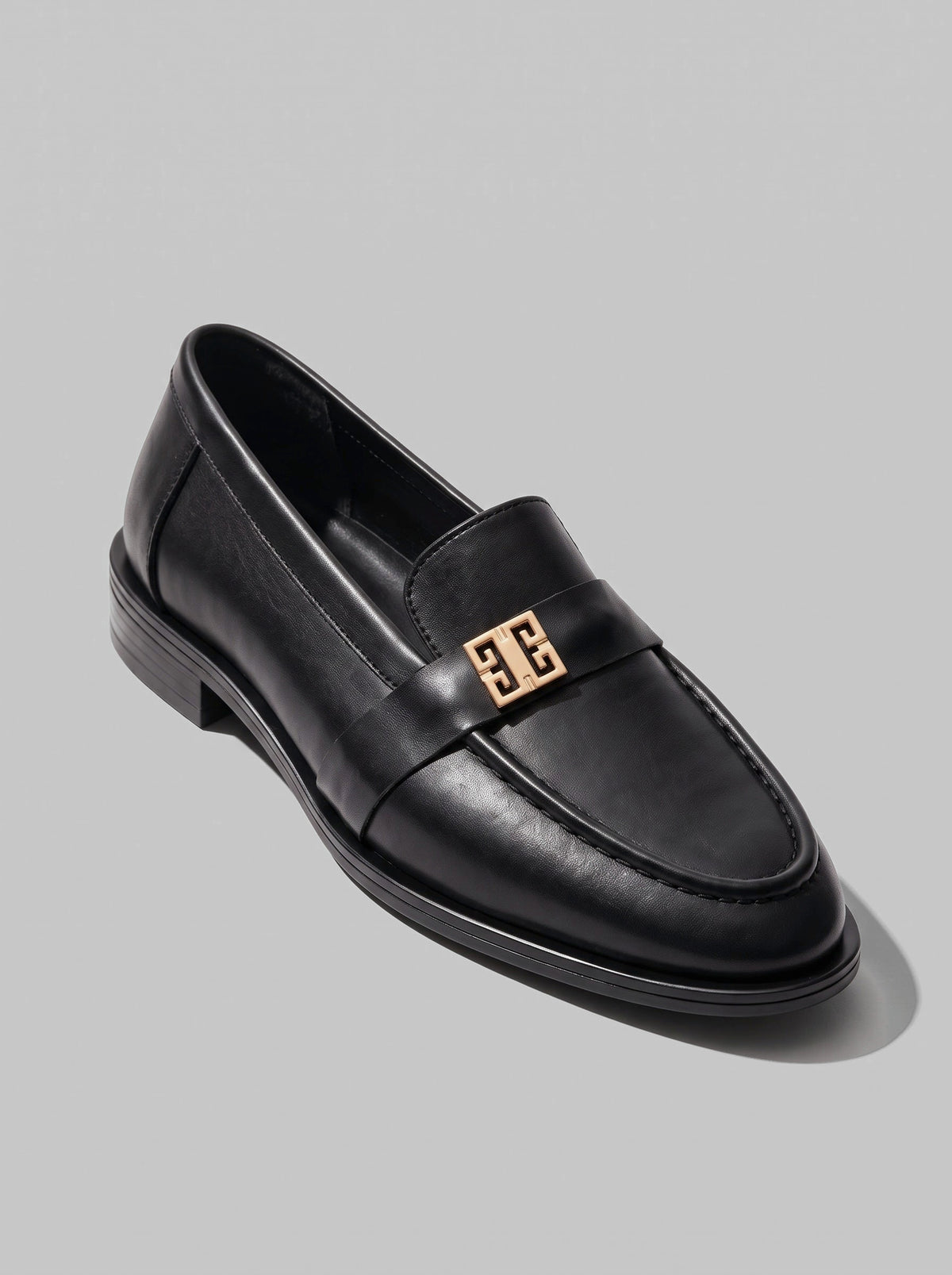 Volterra Black - מוקסין עור שחור עם רצועה רחבה בחזית ועיטור מתכתי זהוב, תפר מודגש סביב החרטום וסוליה דקה.