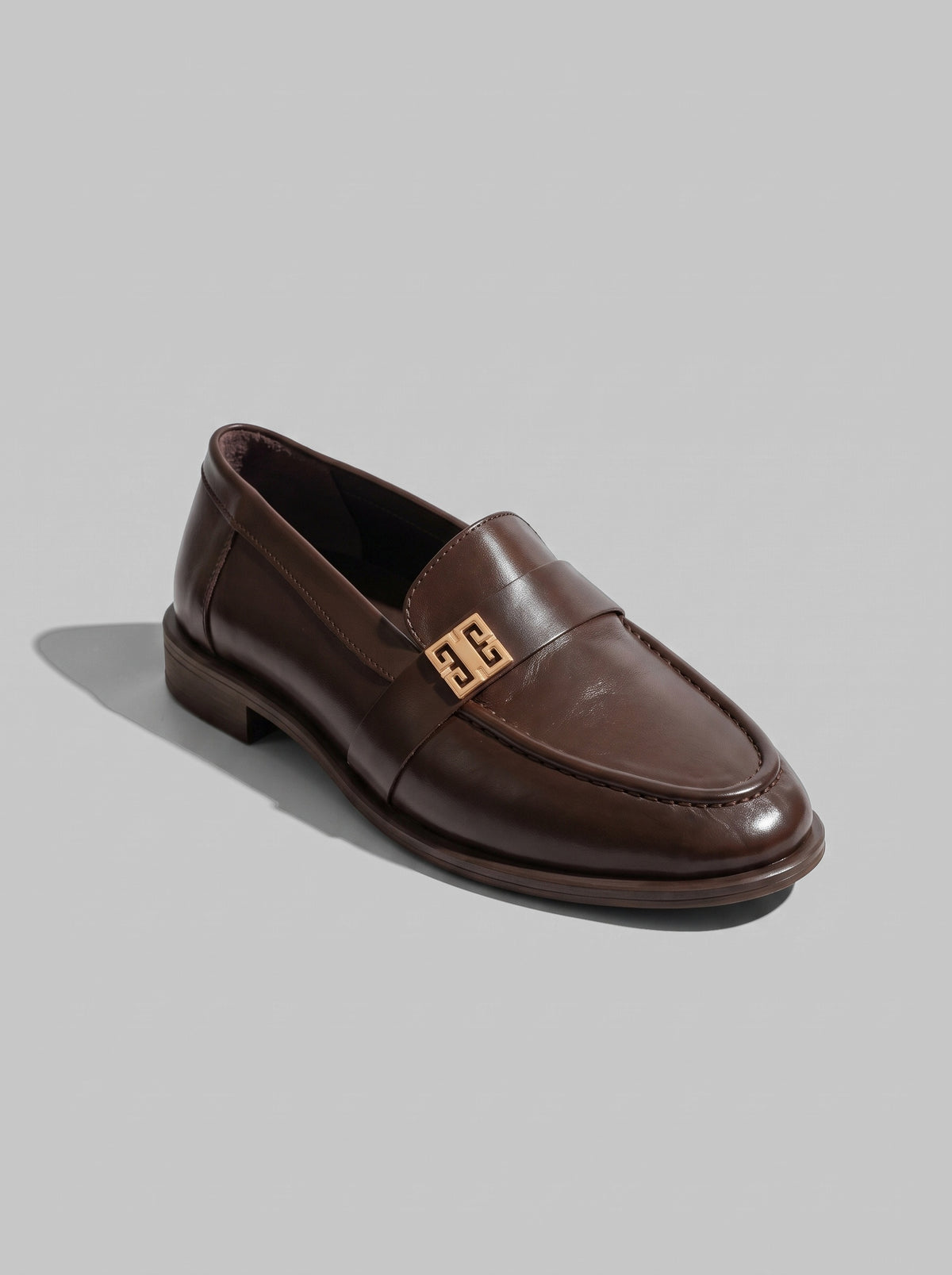 Volterra Dark Brown - מוקסין עור בחום כהה עם רצועה רחבה בחזית ועיטור מתכתי זהוב, תפר מודגש סביב החרטום וסוליה דקה.