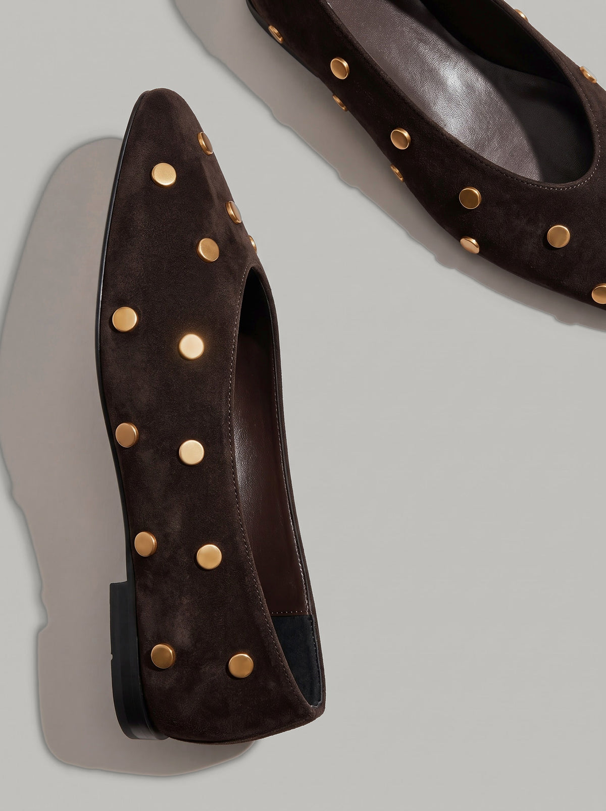Aurelia Chocolate Brown - נעל בלרינה מזמש בחום שוקולד עם חרטום מעוגל ועיטורי ניטים עגולים בגוון זהב על הגפה.